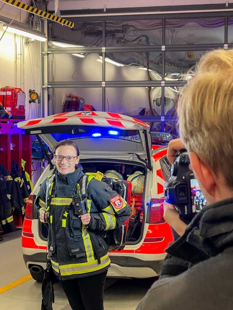 Portraitshooting im Gerätehaus: Feuerwehrfrau posiert vor einem Einsatzfahrzeug mit geöffneter Heckklappe.