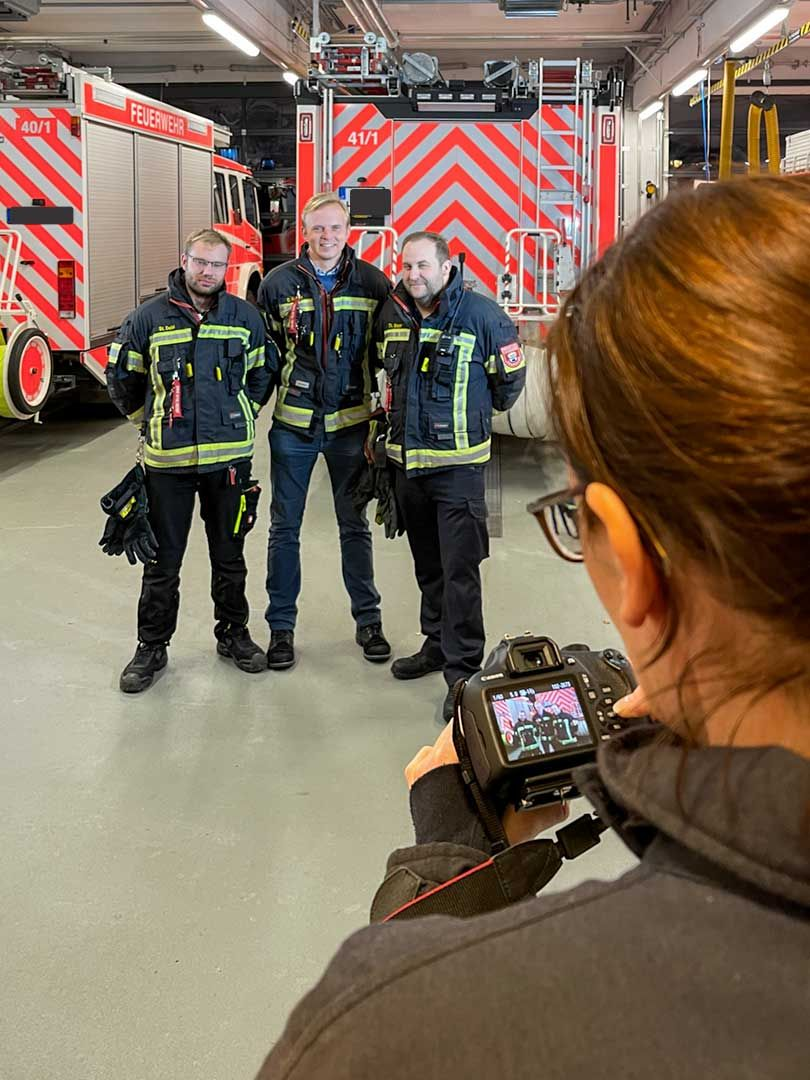 Teilnehmerin fotografiert drei Feuerwehrleute in Einsatzkleidung vor den Löschfahrzeugen im Gerätehaus.